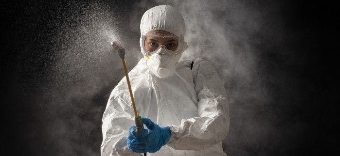 A person suited up with a sprayer 
