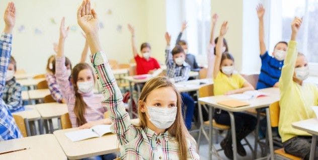 Masked school children in class with hands in the air