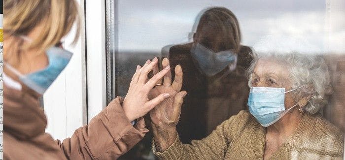 A long-term care resident touching hands through a glass window during COVID-19 lockdowns. 