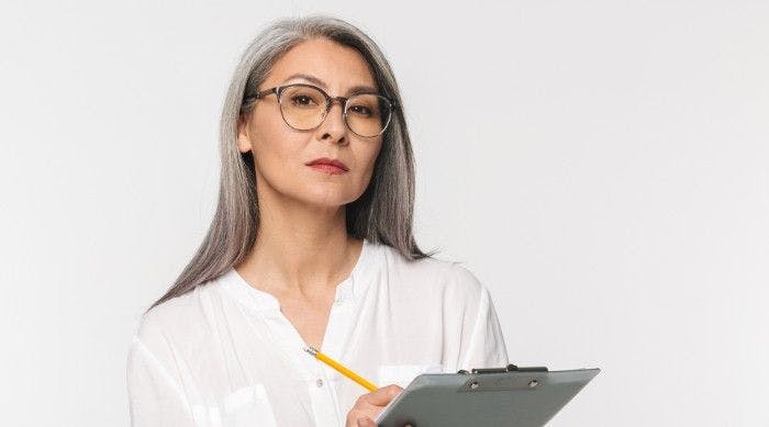 white-haired lady holding a clipboard looking stern