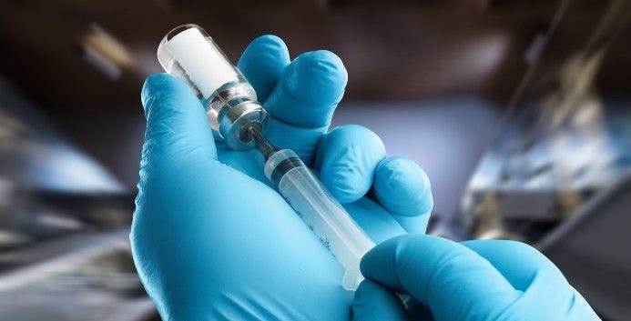 Gloved hand holding vaccine bottle, needle